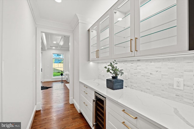 bar with wine cooler, light stone counters, dark hardwood / wood-style flooring, white cabinets, and ornamental molding