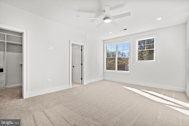 unfurnished bedroom with light carpet, a closet, a spacious closet, and ceiling fan