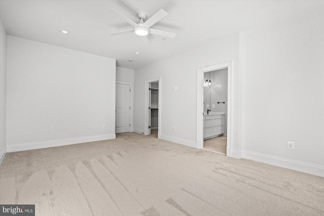 unfurnished bedroom featuring light carpet, a walk in closet, ensuite bathroom, and ceiling fan