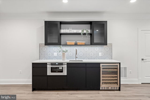 bar featuring stainless steel oven, sink, wine cooler, light hardwood / wood-style flooring, and tasteful backsplash