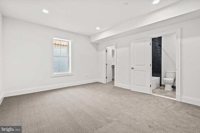 unfurnished bedroom with connected bathroom, a walk in closet, and light colored carpet