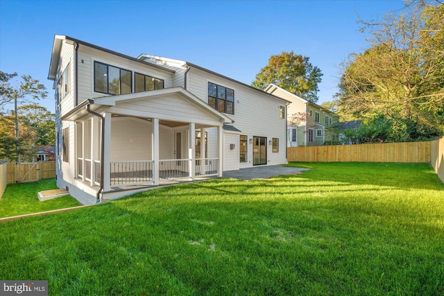 rear view of property featuring a lawn, a sunroom, and a patio