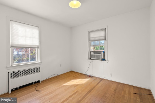 unfurnished room with radiator heating unit, cooling unit, and wood-type flooring