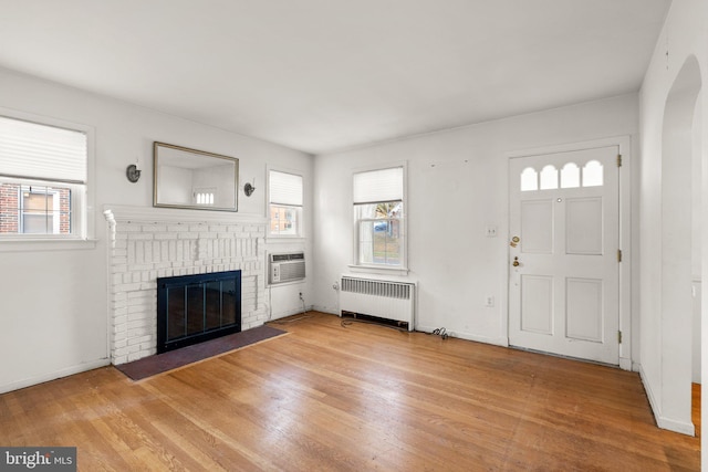 foyer entrance featuring a brick fireplace, radiator heating unit, a wall mounted AC, and light hardwood / wood-style flooring