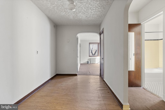 hall with radiator heating unit, wood-type flooring, and a textured ceiling