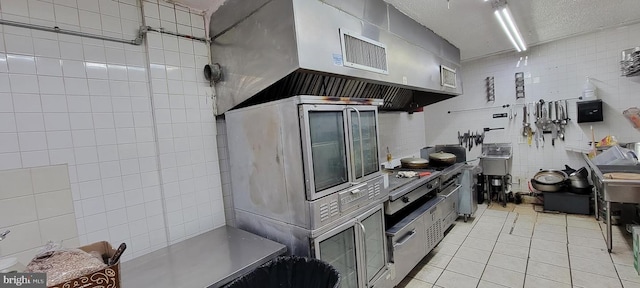 kitchen with sink, ventilation hood, a textured ceiling, light tile patterned floors, and tile walls