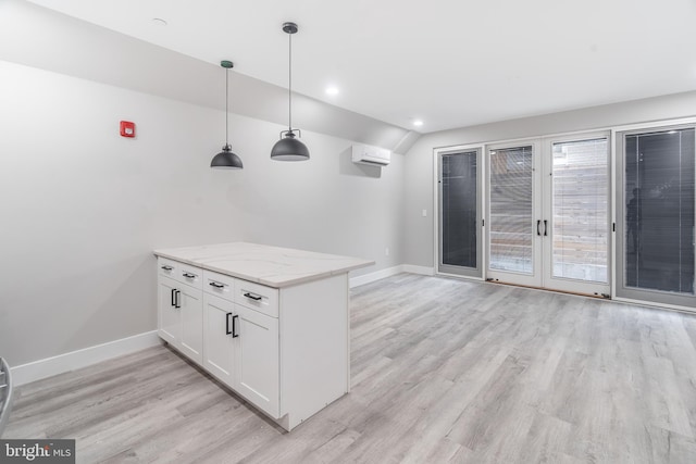 kitchen with hanging light fixtures, light hardwood / wood-style flooring, white cabinetry, light stone counters, and a wall mounted AC