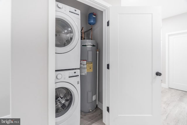 laundry room with electric water heater, stacked washer / dryer, and light wood-type flooring