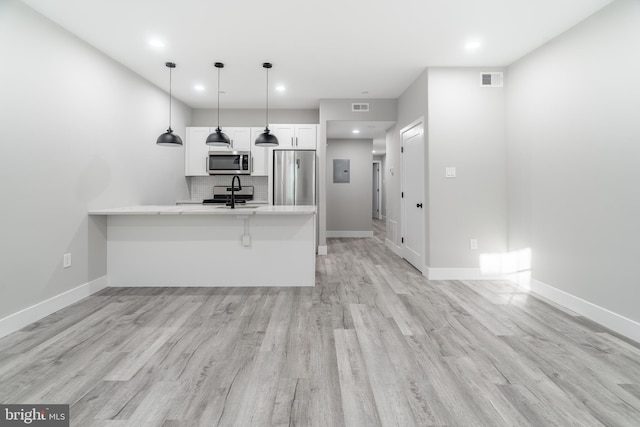 kitchen with appliances with stainless steel finishes, a breakfast bar, white cabinets, backsplash, and light hardwood / wood-style flooring