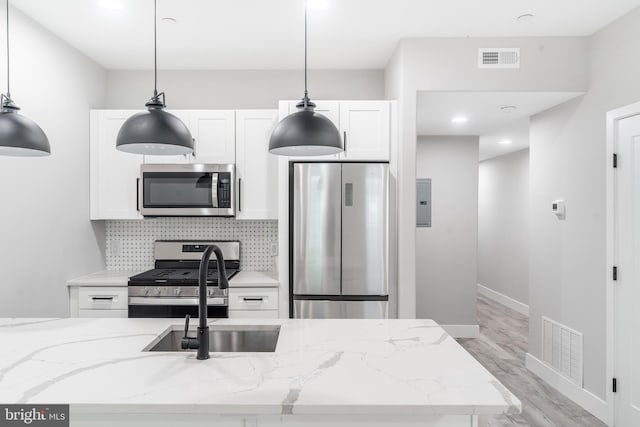 kitchen with appliances with stainless steel finishes, tasteful backsplash, light wood-type flooring, white cabinetry, and pendant lighting