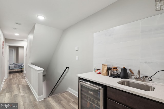 bar with dark brown cabinetry, light wood-type flooring, sink, and beverage cooler