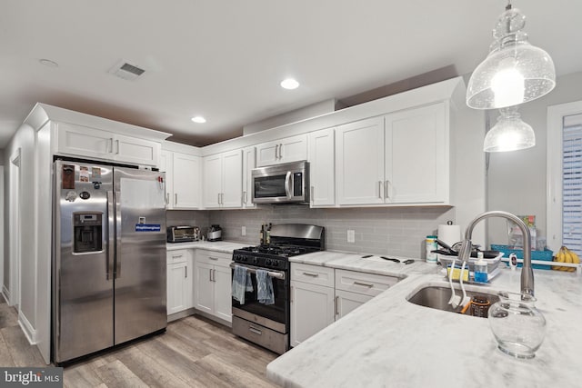 kitchen featuring light hardwood / wood-style flooring, white cabinets, stainless steel appliances, and decorative light fixtures