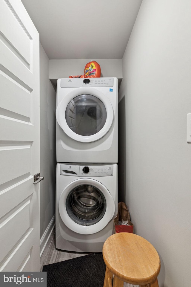 clothes washing area with hardwood / wood-style floors and stacked washer / drying machine