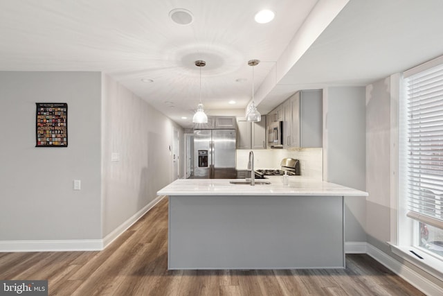 kitchen featuring gray cabinetry, dark hardwood / wood-style floors, appliances with stainless steel finishes, decorative light fixtures, and kitchen peninsula