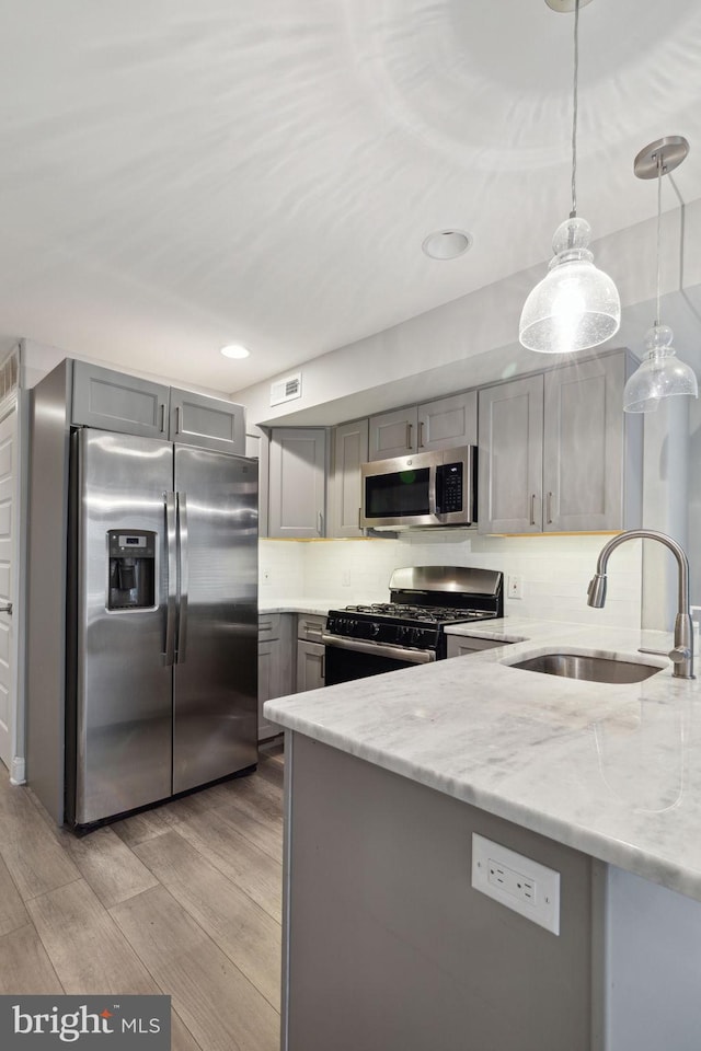 kitchen with sink, light wood-type flooring, appliances with stainless steel finishes, decorative light fixtures, and light stone counters