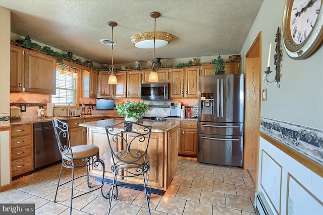 kitchen featuring a center island, sink, decorative light fixtures, light stone counters, and stainless steel appliances