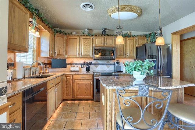 kitchen with sink, a center island, light stone counters, decorative light fixtures, and black appliances