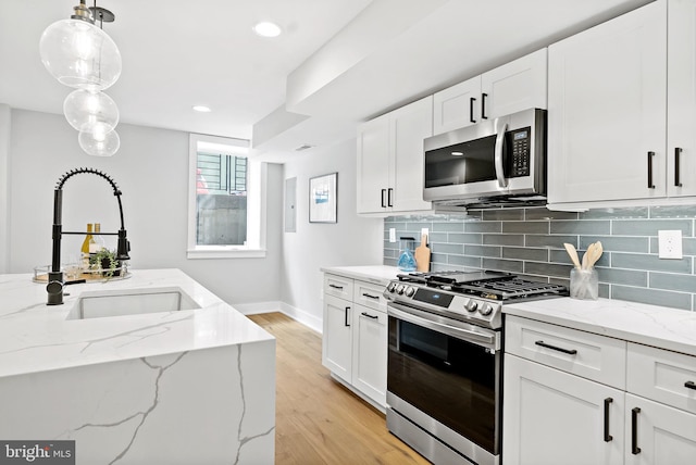 kitchen featuring light stone countertops, hanging light fixtures, white cabinets, and stainless steel appliances