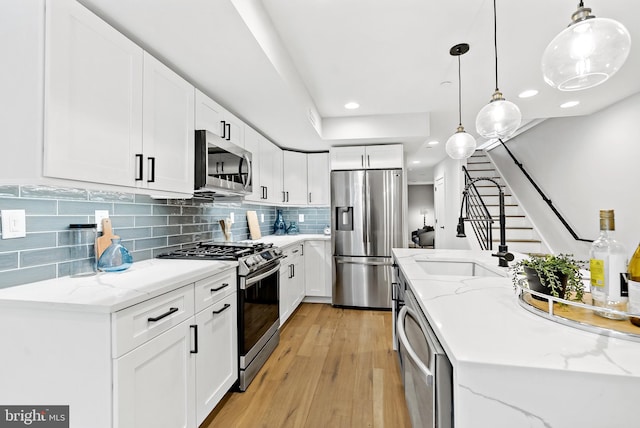 kitchen featuring light stone countertops, white cabinets, pendant lighting, and appliances with stainless steel finishes