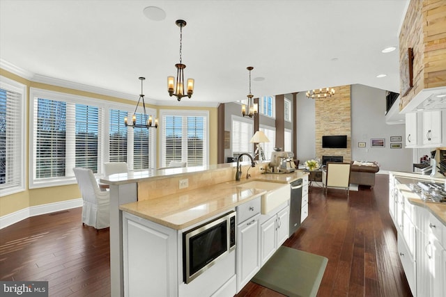 kitchen with sink, hanging light fixtures, a stone fireplace, white cabinets, and appliances with stainless steel finishes