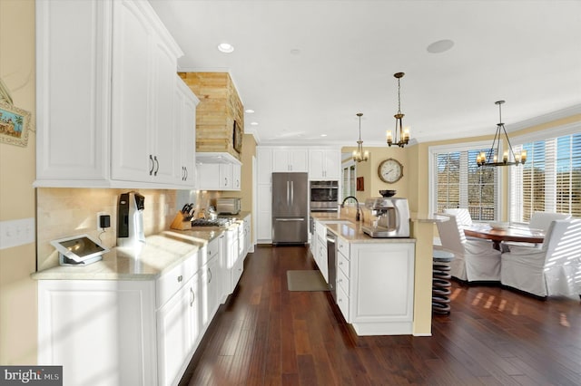 kitchen with a center island with sink, appliances with stainless steel finishes, tasteful backsplash, decorative light fixtures, and white cabinetry