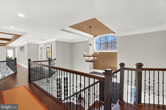 corridor featuring a raised ceiling, crown molding, dark wood-type flooring, and a chandelier