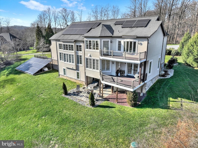 rear view of property with solar panels, a balcony, a lawn, and a wooden deck