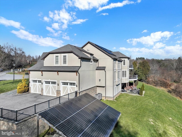 exterior space with solar panels, a garage, cooling unit, and a lawn