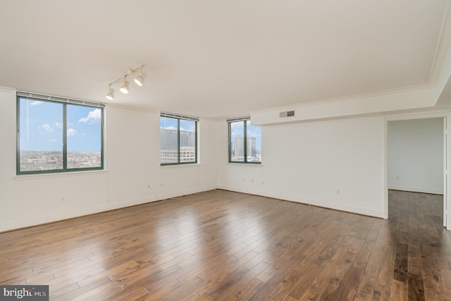 empty room featuring crown molding, dark hardwood / wood-style floors, and rail lighting