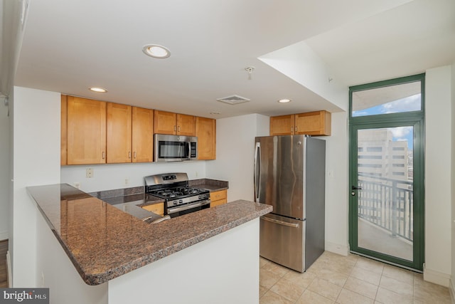 kitchen with kitchen peninsula, appliances with stainless steel finishes, light tile floors, and dark stone countertops