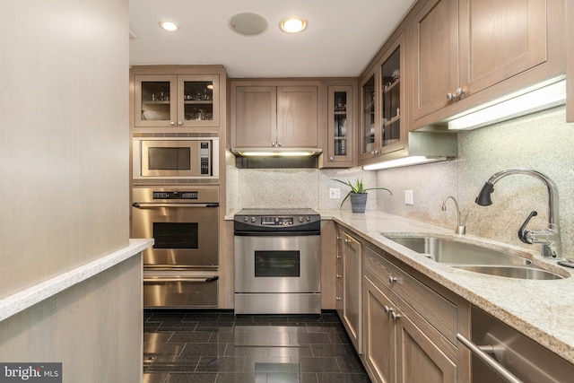 kitchen with light stone countertops, appliances with stainless steel finishes, backsplash, dark tile floors, and sink