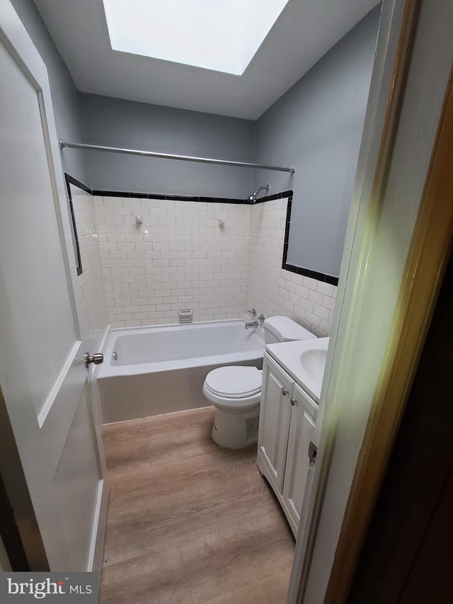 full bathroom featuring vanity, a skylight, hardwood / wood-style flooring, tiled shower / bath combo, and toilet