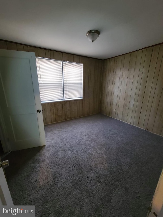 spare room featuring dark colored carpet and wooden walls