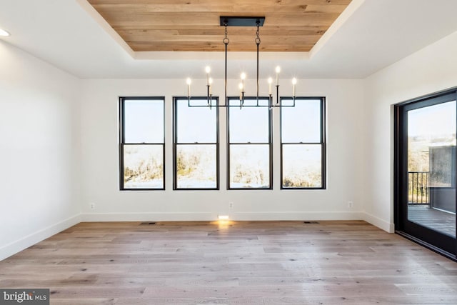 unfurnished dining area with a tray ceiling, light hardwood / wood-style flooring, and a notable chandelier