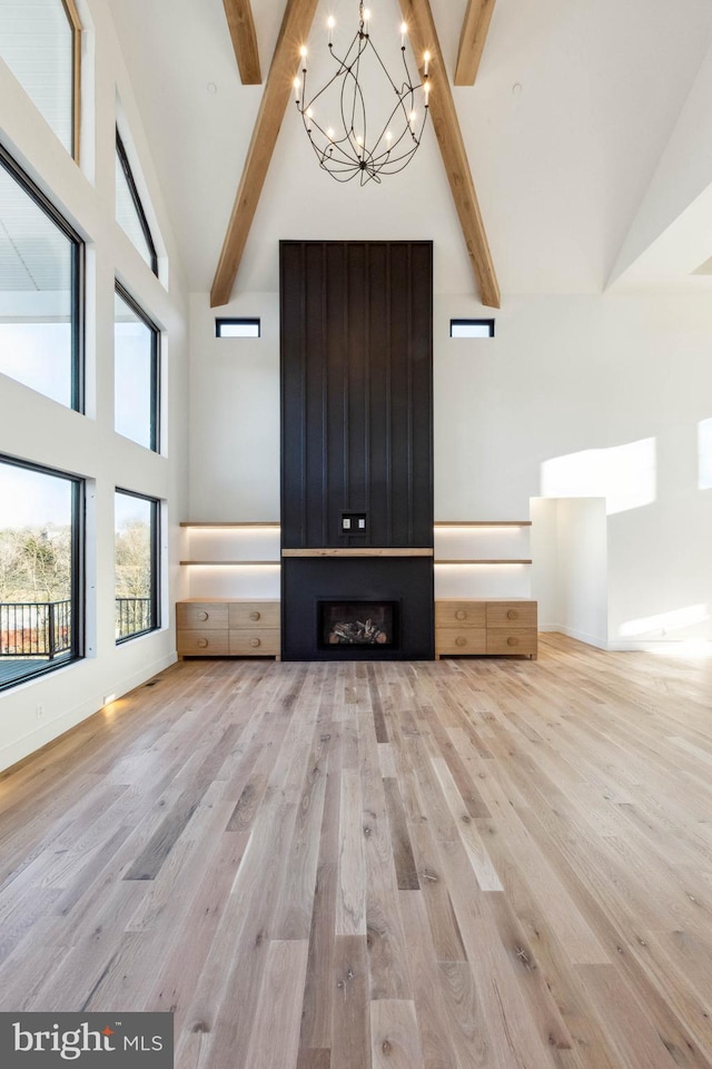 unfurnished living room with beamed ceiling, light wood-type flooring, a chandelier, and high vaulted ceiling