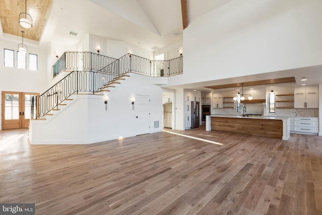 unfurnished living room with hardwood / wood-style flooring, sink, and high vaulted ceiling