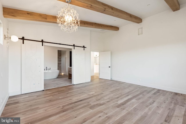 unfurnished bedroom featuring light hardwood / wood-style flooring, ensuite bath, a barn door, beamed ceiling, and a notable chandelier