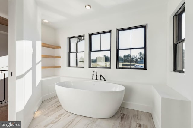 bathroom with a wealth of natural light, hardwood / wood-style floors, and a bath