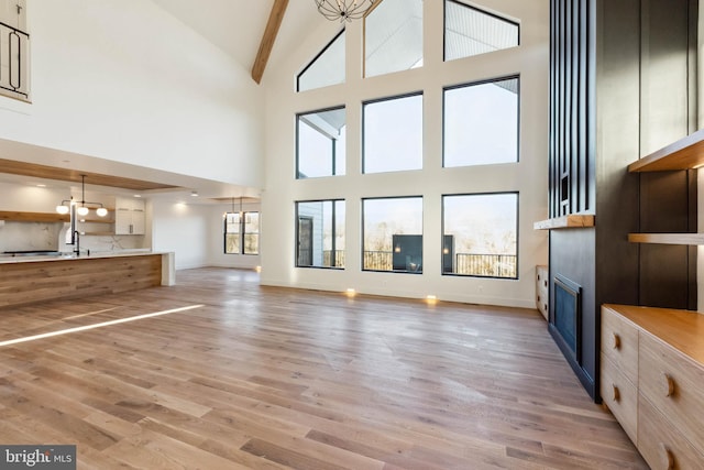 unfurnished living room with beamed ceiling, light wood-type flooring, and high vaulted ceiling