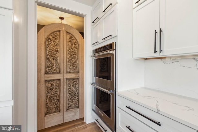 kitchen with light stone counters, double oven, decorative backsplash, white cabinets, and light wood-type flooring