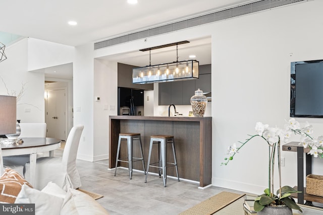 kitchen featuring black refrigerator with ice dispenser, sink, decorative light fixtures, a kitchen bar, and kitchen peninsula