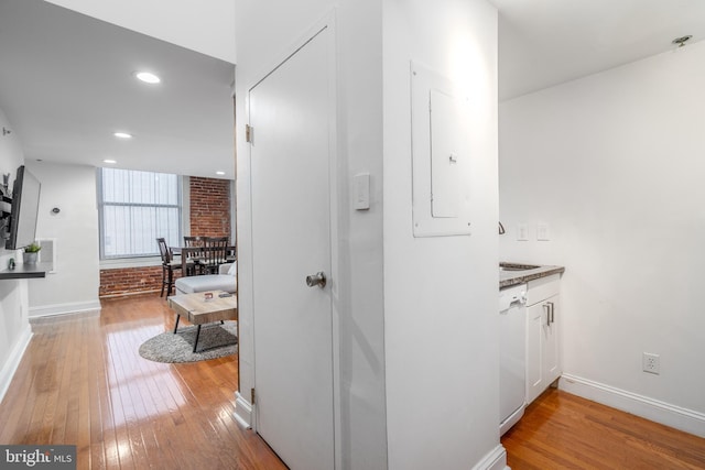 hallway with electric panel, hardwood / wood-style flooring, and brick wall