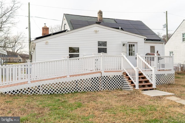 rear view of property featuring a lawn, solar panels, and a deck