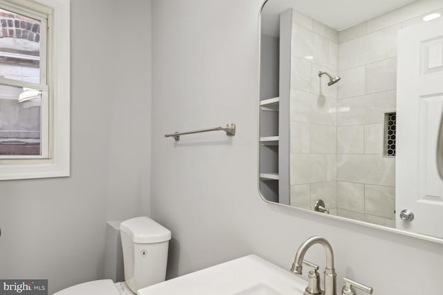 bathroom with a tile shower, toilet, and sink