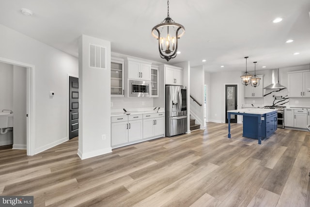 kitchen featuring decorative light fixtures, light hardwood / wood-style floors, white cabinetry, stainless steel appliances, and wall chimney range hood