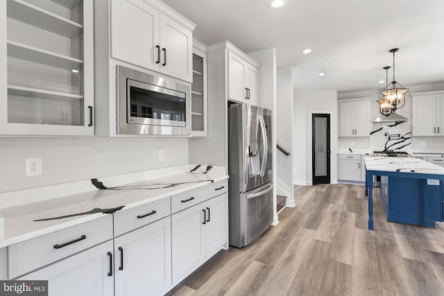 kitchen with stainless steel appliances, decorative light fixtures, light stone countertops, white cabinetry, and light wood-type flooring