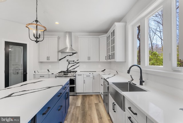 kitchen with appliances with stainless steel finishes, light hardwood / wood-style floors, white cabinetry, pendant lighting, and wall chimney range hood