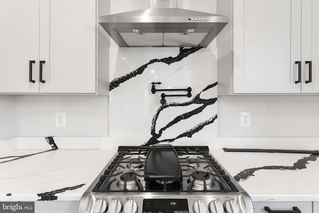 kitchen with stove, wall chimney exhaust hood, white cabinetry, and light stone countertops