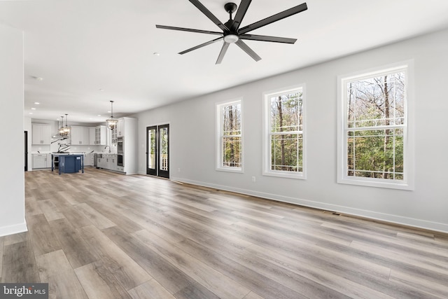 unfurnished living room with french doors, ceiling fan with notable chandelier, light wood-type flooring, and plenty of natural light