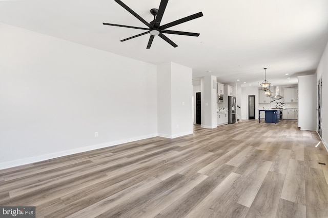 unfurnished living room featuring light wood-type flooring and ceiling fan with notable chandelier